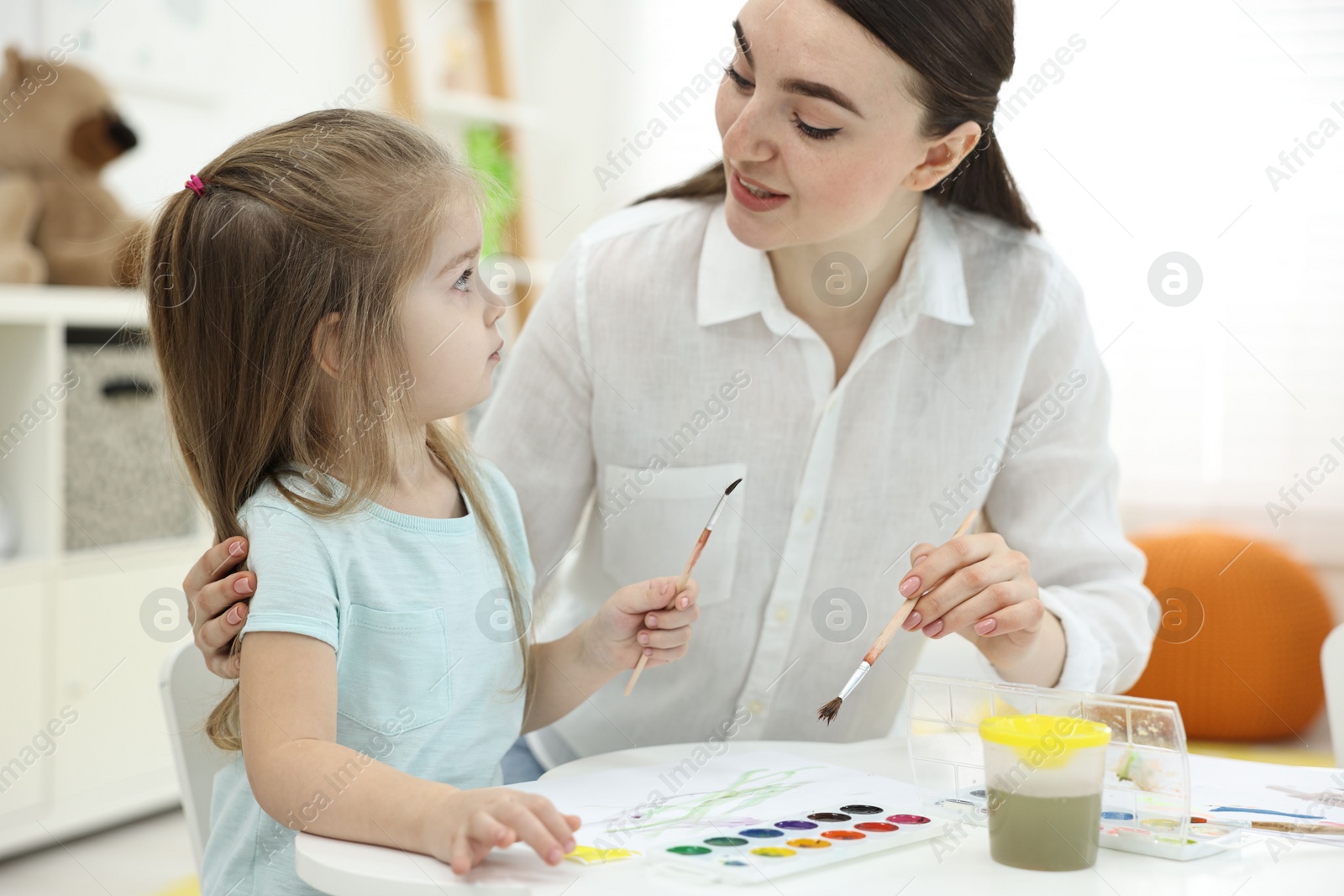 Photo of Mother and her little daughter painting with watercolor at home