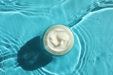 Photo of Jar with moisturizing cream in water on light blue background, top view