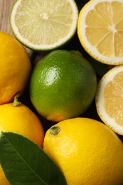 Fresh ripe lemons, limes and green leaf as background, closeup