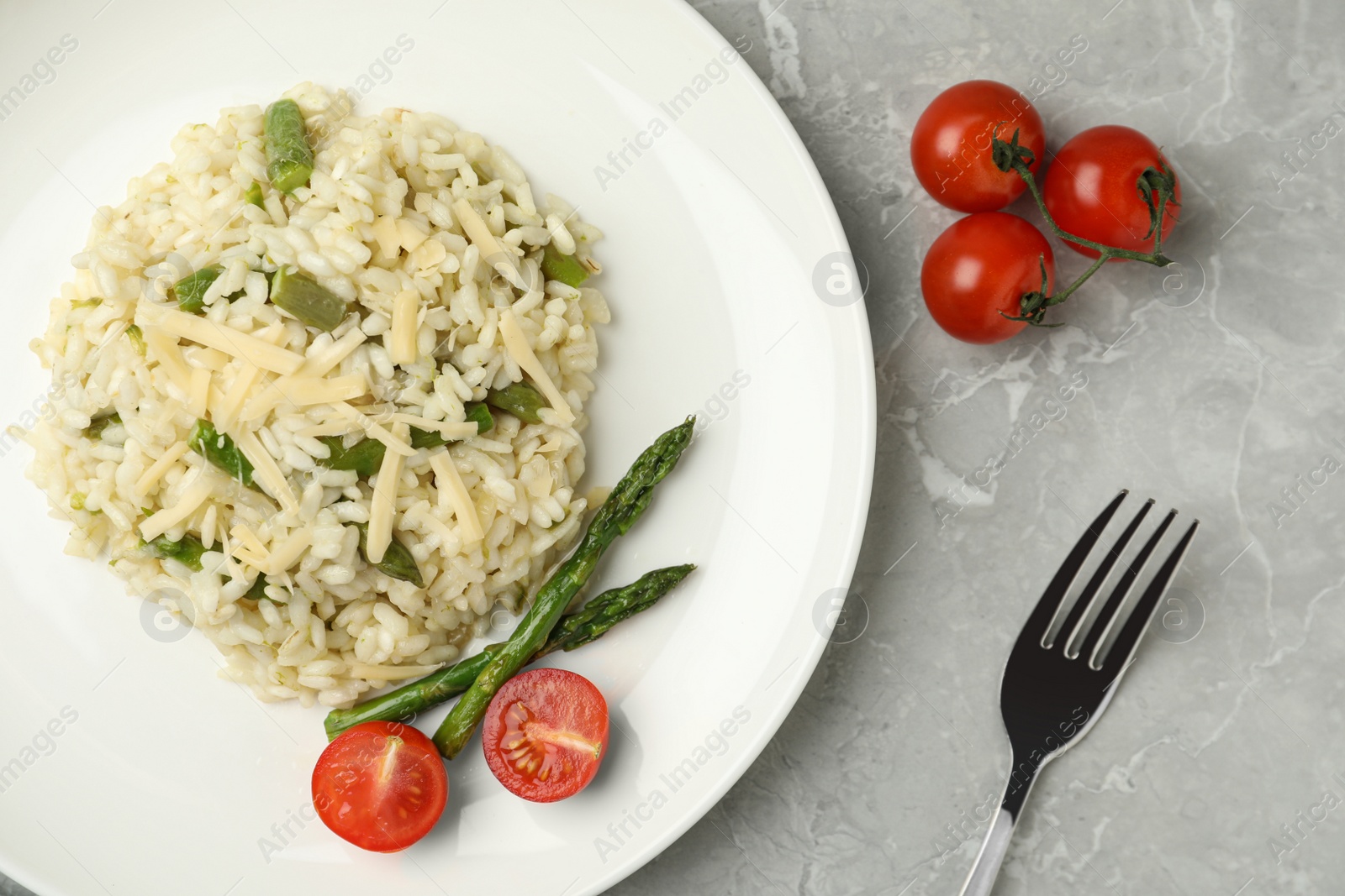 Photo of Delicious risotto with asparagus and tomatoes on grey marble table, flat lay