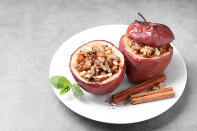 Photo of Tasty baked apples with nuts, honey, cinnamon sticks and mint on gray table