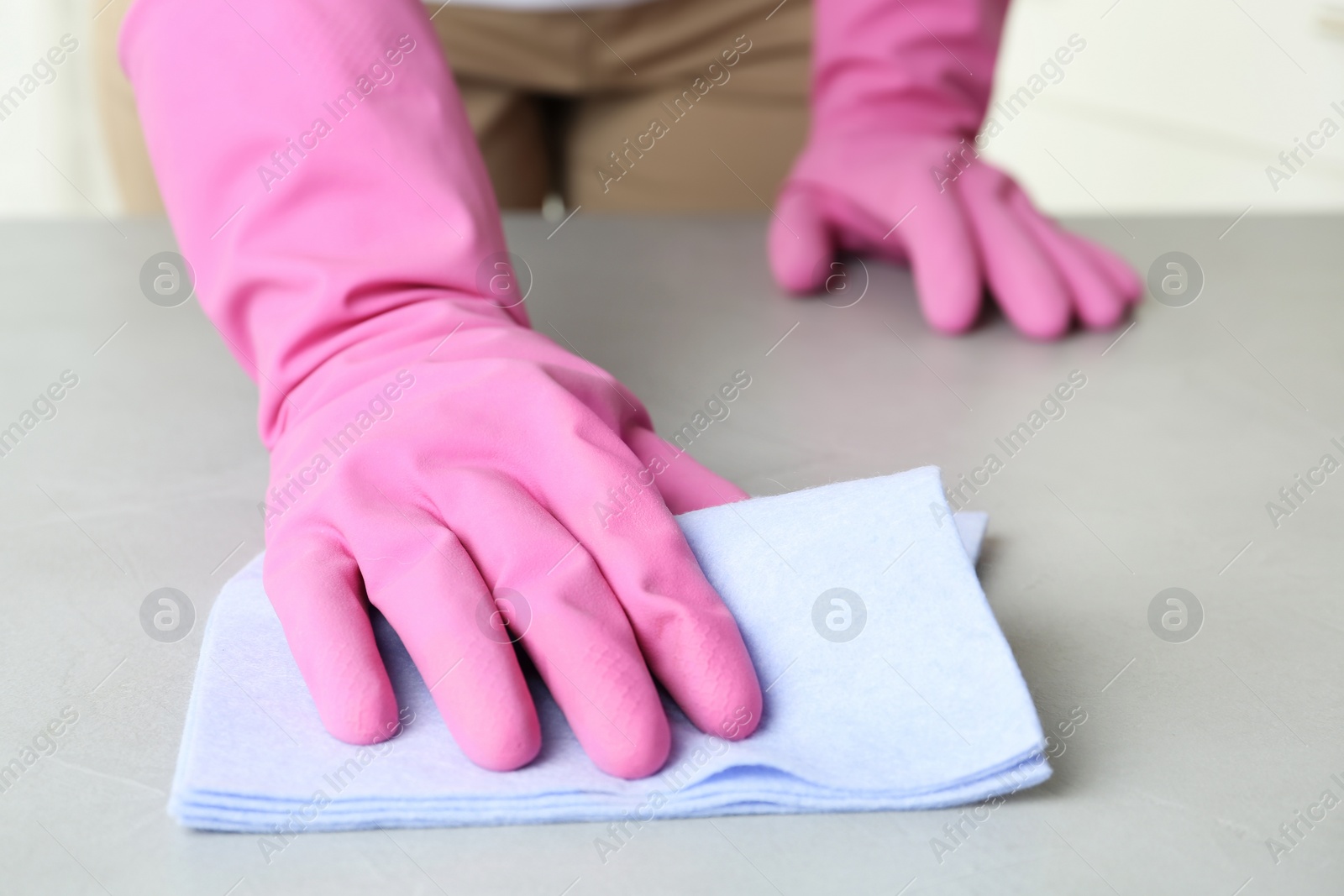 Photo of Woman in gloves wiping grey table with rag indoors, closeup