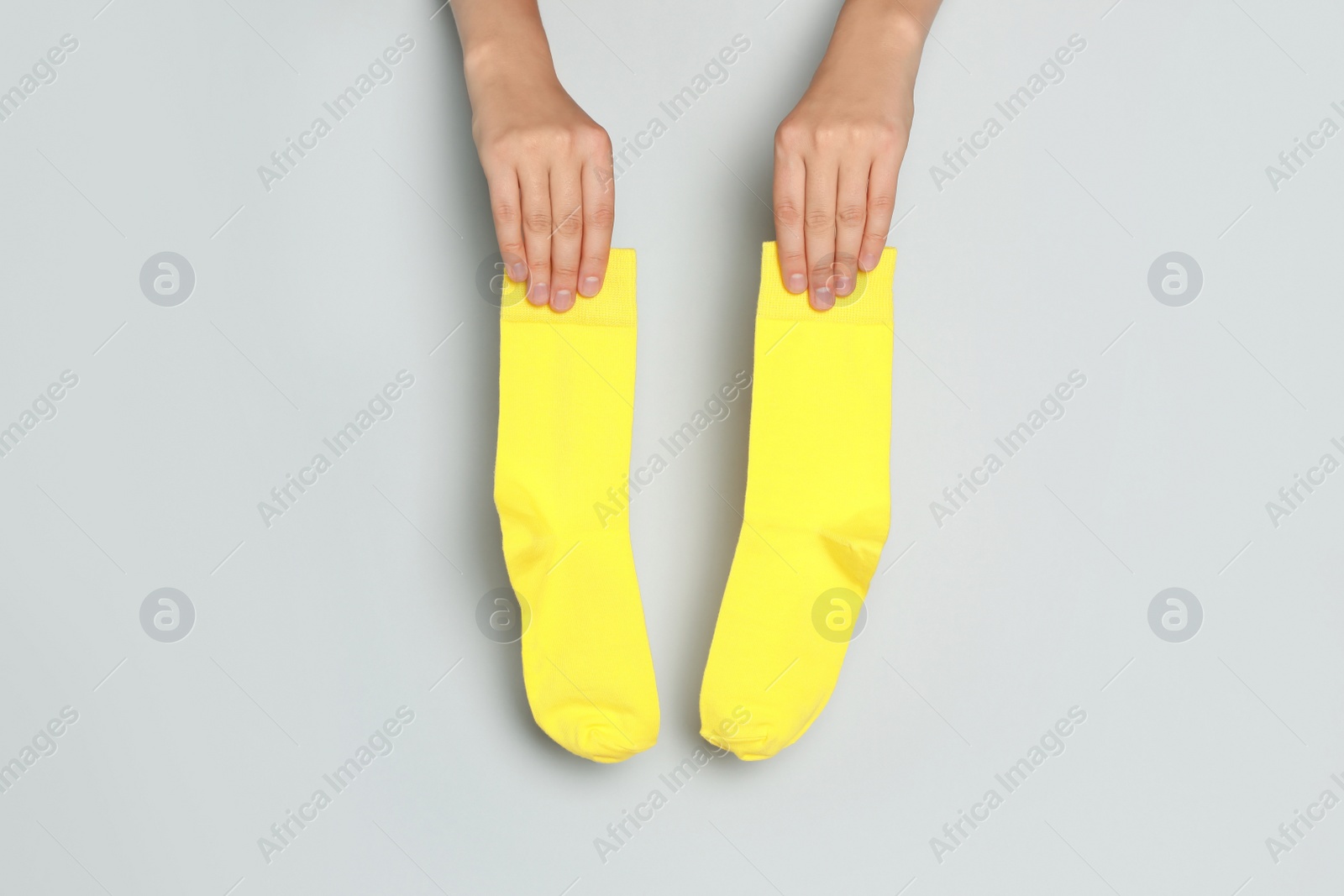 Photo of Woman holding pair of yellow socks on grey background, closeup