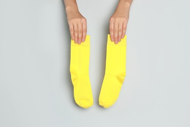 Photo of Woman holding pair of yellow socks on grey background, closeup
