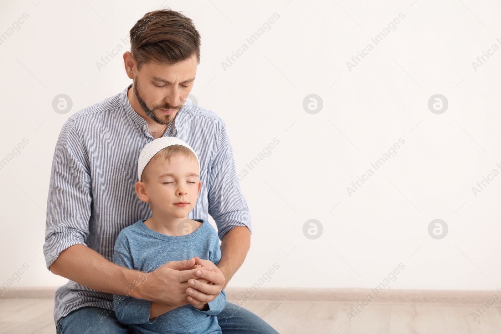 Photo of Muslim man and his son praying together indoors. Space for text