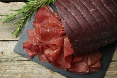 Photo of Tasty bresaola and rosemary on wooden table, top view