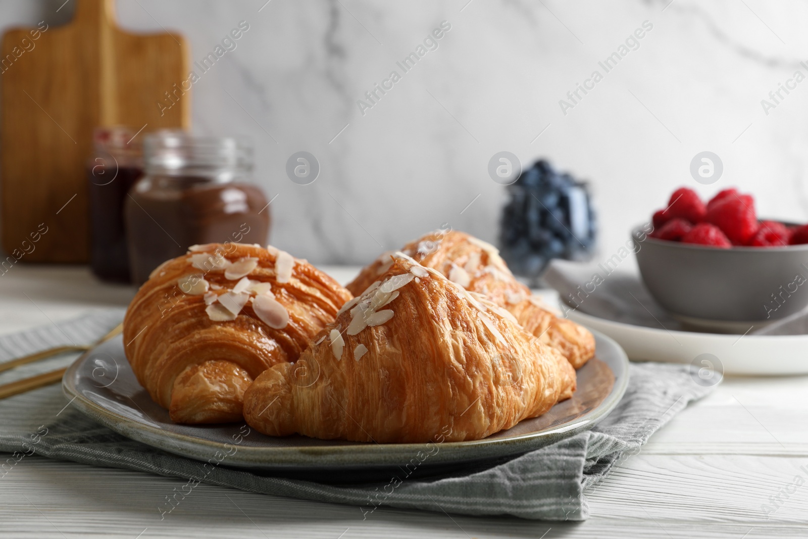 Delicious croissants with almond flakes on white wooden table, closeup Photo of Delicious croissants with almond flakes on white wooden table, closeup