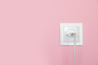 Photo of Charger adapter plugged into power socket on pink wall, space for text. Electrical supply