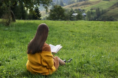 Photo of Young woman reading book on green meadow, back view