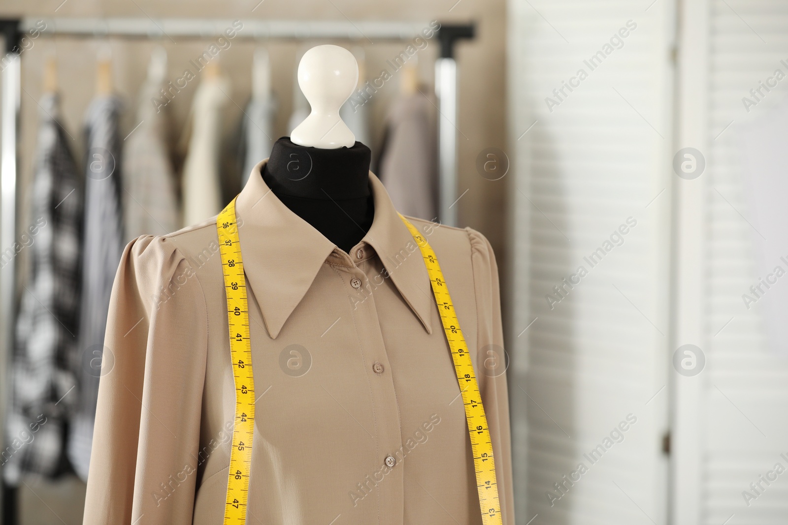 Photo of Mannequin with shirt and measuring tape in tailor shop, space for text