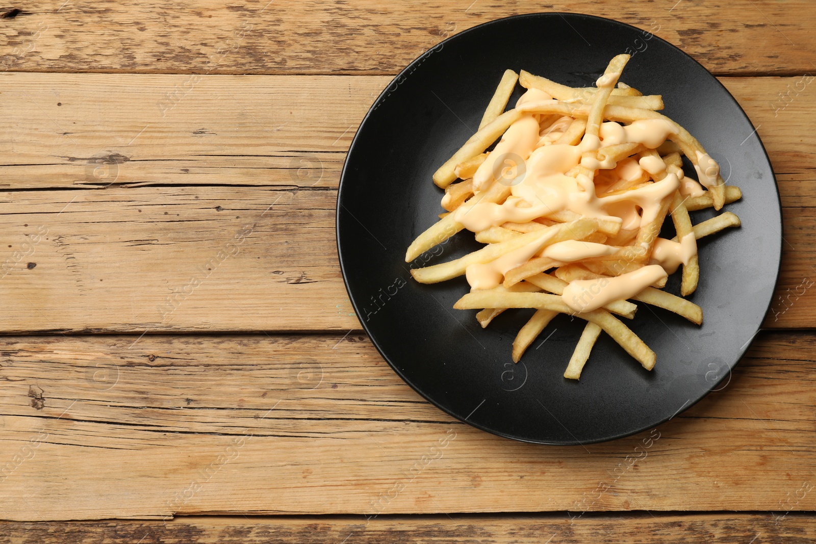 Photo of Delicious French fries with cheese sauce on wooden table, top view. Space for text