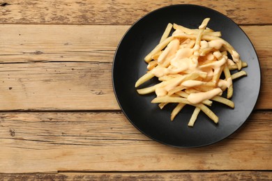 Delicious French fries with cheese sauce on wooden table, top view. Space for text