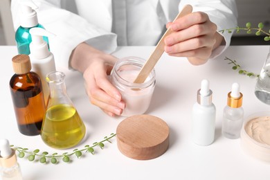 Photo of Dermatologist with jar testing cosmetic product at white table indoors, closeup