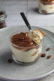 Photo of Delicious tiramisu in glass, coffee beans and spoon on table