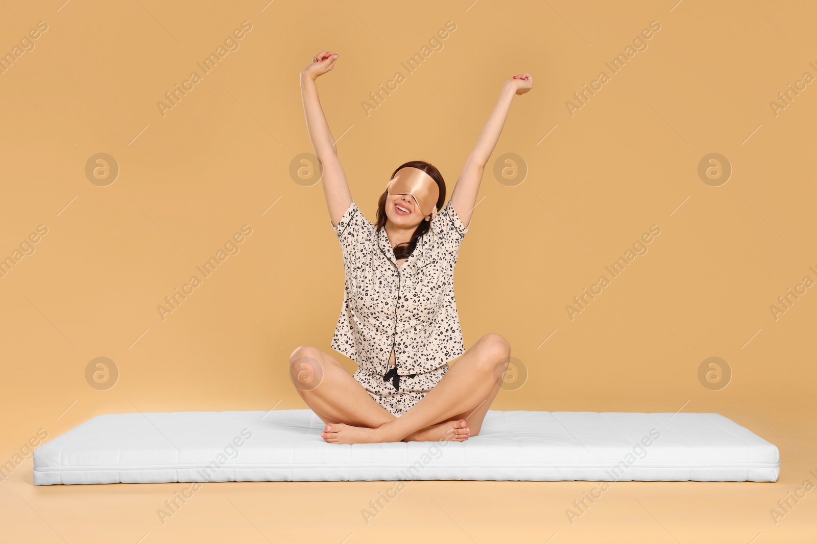Photo of Woman in sleep mask stretching on soft mattress against beige background