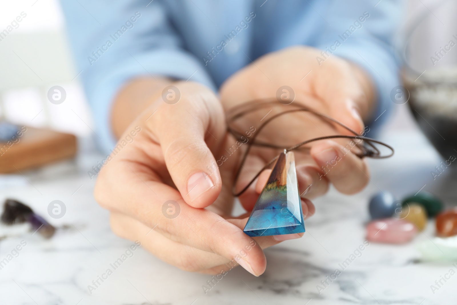 Photo of Woman holding handmade gemstone amulet at table, closeup