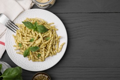Photo of Plate of delicious trofie pasta with pesto sauce and basil leaves on grey wooden table, flat lay. Space for text