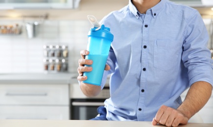 Photo of Young man holding bottle of protein shake in kitchen, closeup. Space for text