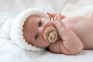 Cute newborn baby in white knitted hat lying on bed, closeup