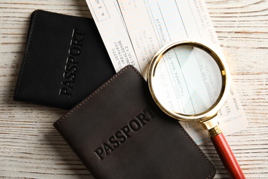 Passports, tickets and magnifying glass on wooden table, top view. Travel agency