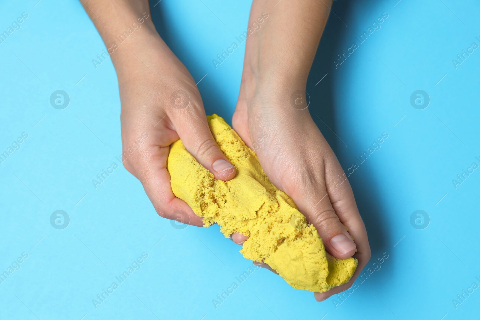 Photo of Woman playing with yellow kinetic sand on light blue background, top view