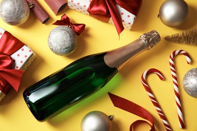 Photo of Christmas composition with bottle of champagne and gifts on color background, top view