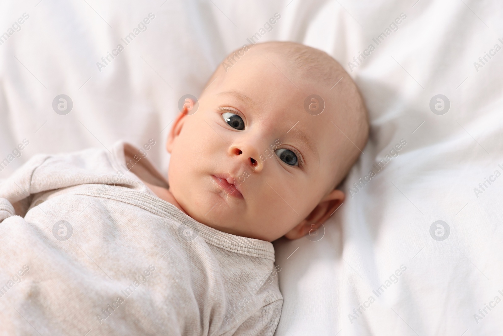 Photo of Cute little baby lying on white sheets, top view