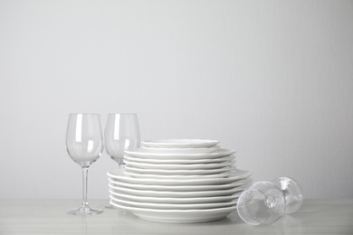 Photo of Stack of clean plates and glasses on table against white background. Space for text