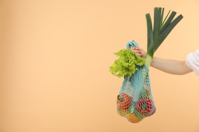 Photo of Woman with string bag of fresh vegetables on beige background, closeup. Space for text