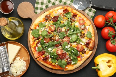 Photo of Delicious vegetarian pizza, ingredients, cutter and grater on black table, flat lay