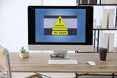 Photo of Computer with warning about virus attack on screen in office