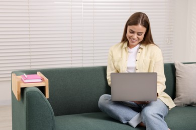 Photo of Happy woman using laptop on sofa with wooden armrest table at home