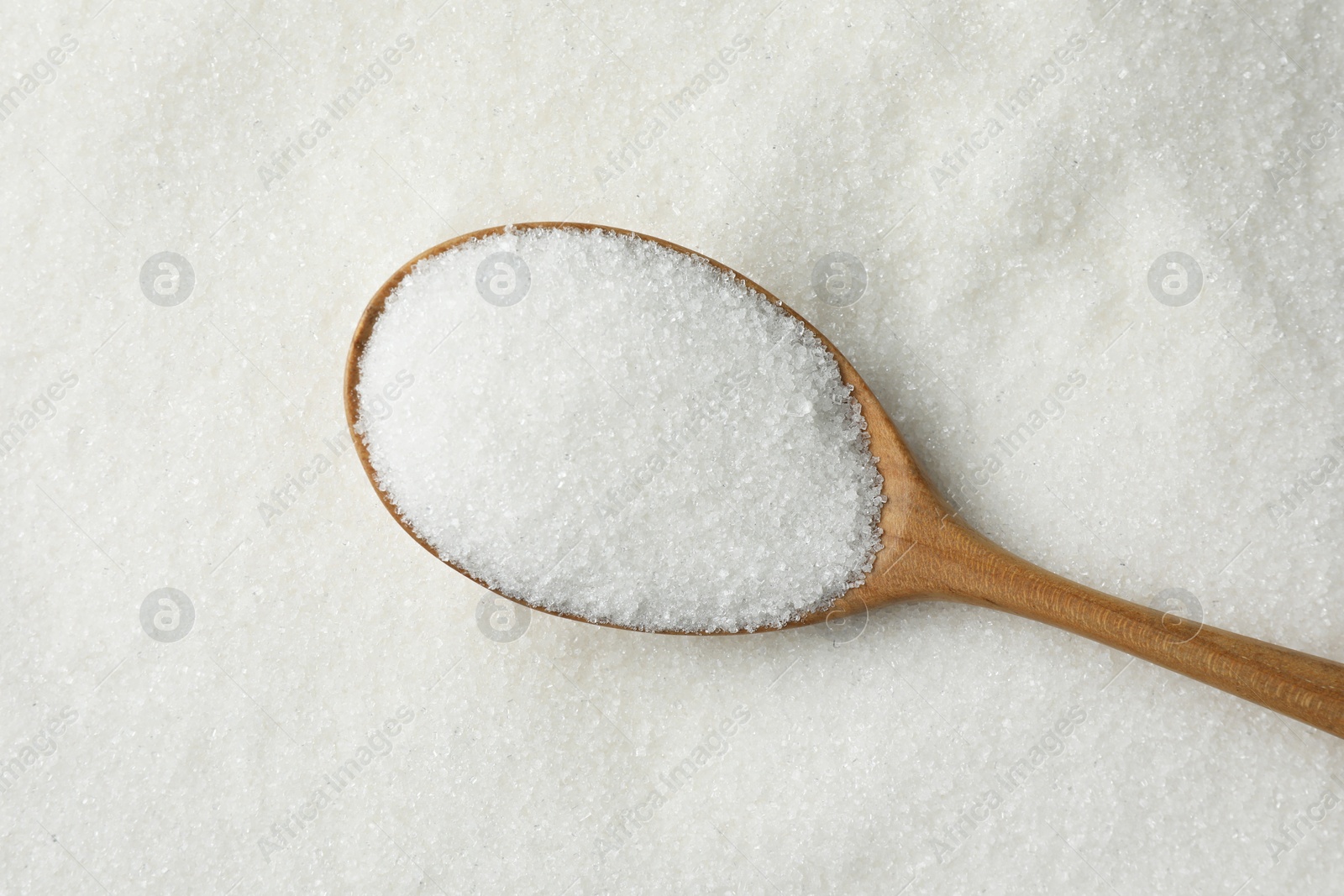 Photo of Wooden spoon on granulated sugar, top view