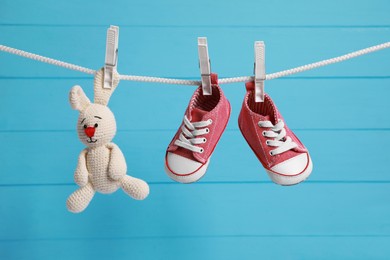 Photo of Cute baby sneakers and crochet toy drying on washing line against light blue wooden wall