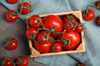 Many ripe red tomatoes in wooden crate on grey table, flat lay