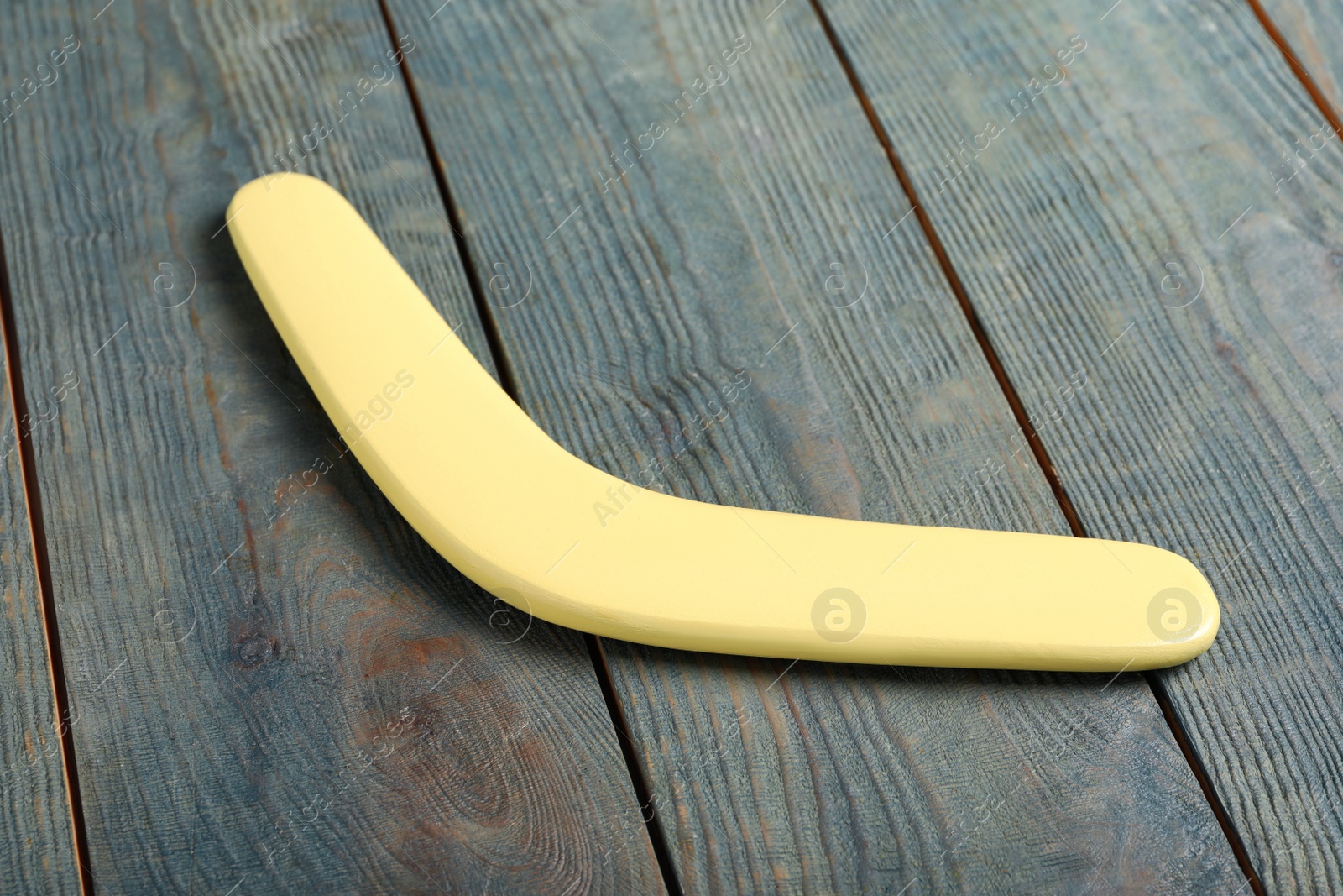 Photo of Yellow boomerang on light blue wooden background. Outdoors activity