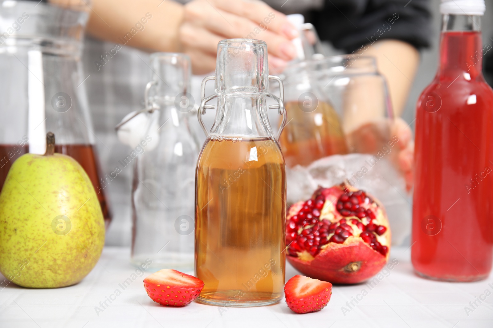 Photo of Making kombucha. Woman putting drink into glass with ice at white tiled table, selective focus