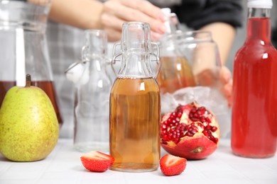 Photo of Making kombucha. Woman putting drink into glass with ice at white tiled table, selective focus