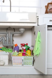 Photo of Open under sink cabinet with different cleaning supplies in kitchen