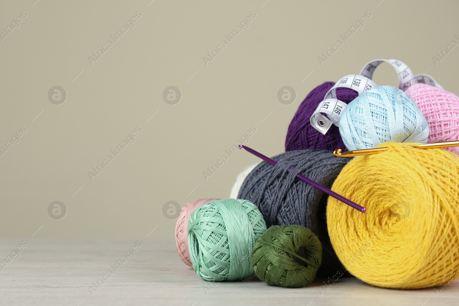 Photo of Clews of colorful knitting threads, crochet hooks and measuring tape on white wooden table against beige background. Space for text