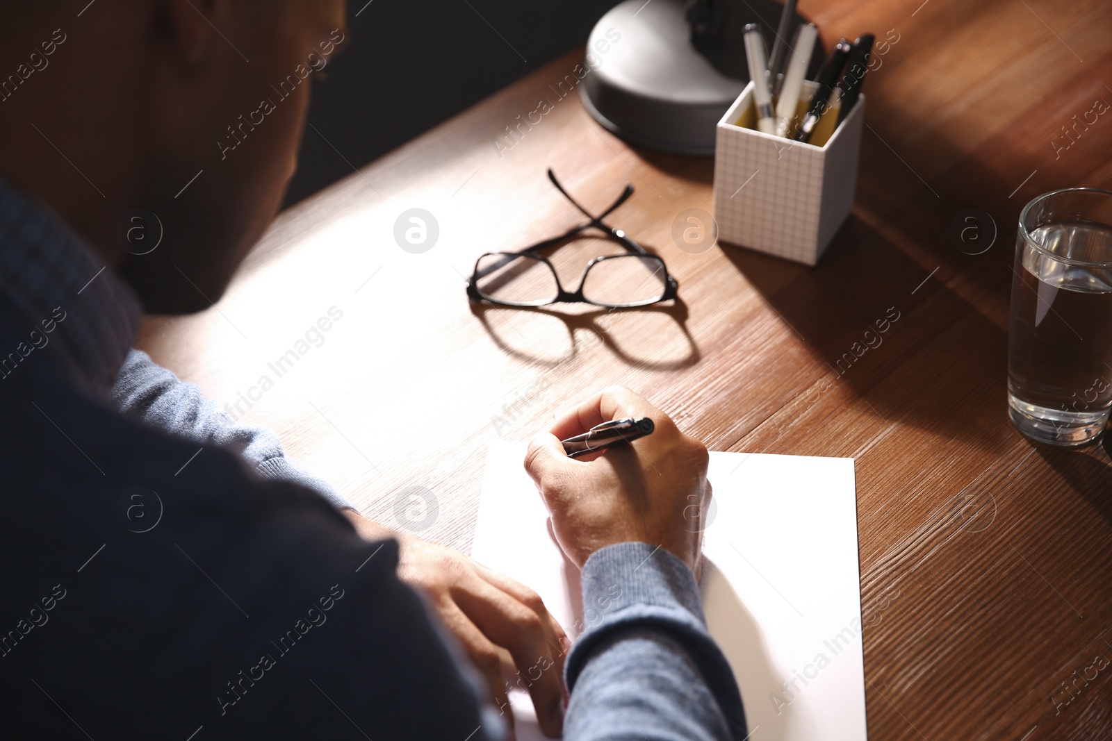 Photo of Man writing letter at wooden table indoors, closeup