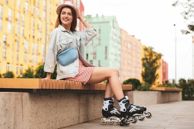 Beautiful young woman with roller skates sitting on bench outdoors