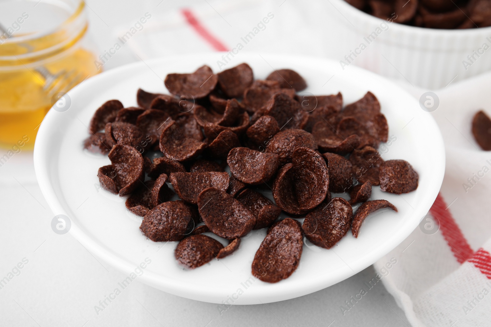 Photo of Breakfast cereal. Chocolate corn flakes and milk in bowl on white table, closeup