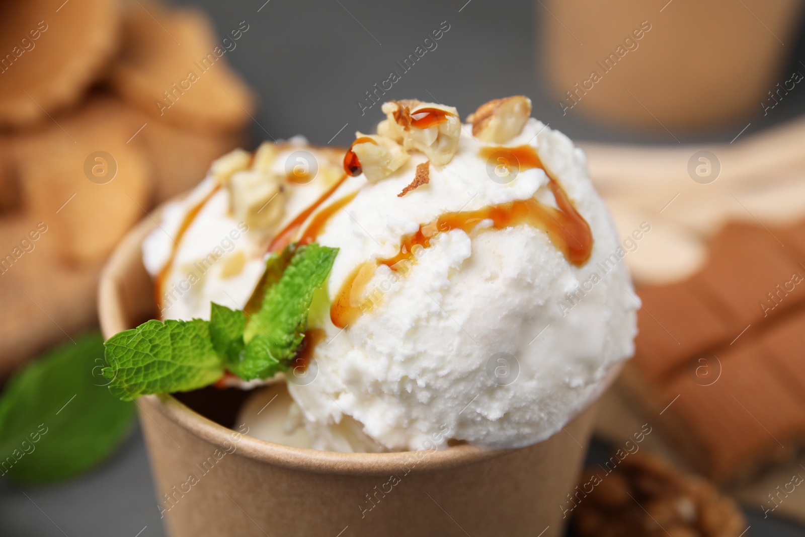 Photo of Tasty ice cream with caramel sauce, mint and nuts in paper cup on table, closeup