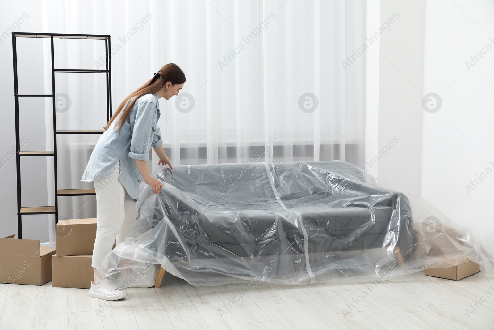 Photo of Young woman putting plastic film away from sofa at home