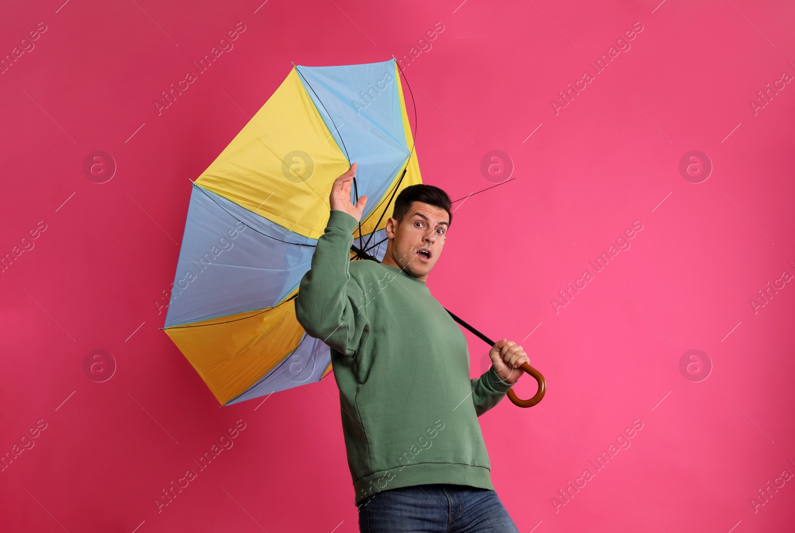 Photo of Emotional man with umbrella caught in gust of wind on pink background