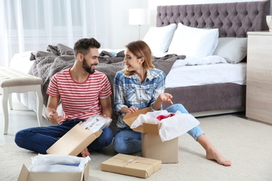 Photo of Young couple opening parcels in bedroom at home