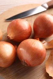Photo of Tray with ripe onions and knife on wooden table, closeup