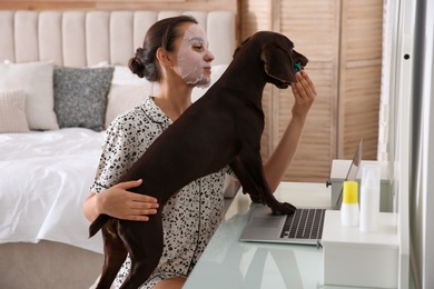 Young woman getting distracted by her dog while working with laptop in home office
