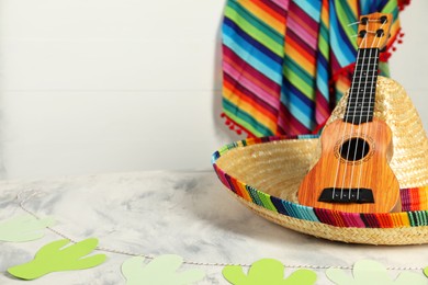 Mexican sombrero hat and ukulele on grey textured table, closeup. Space for text